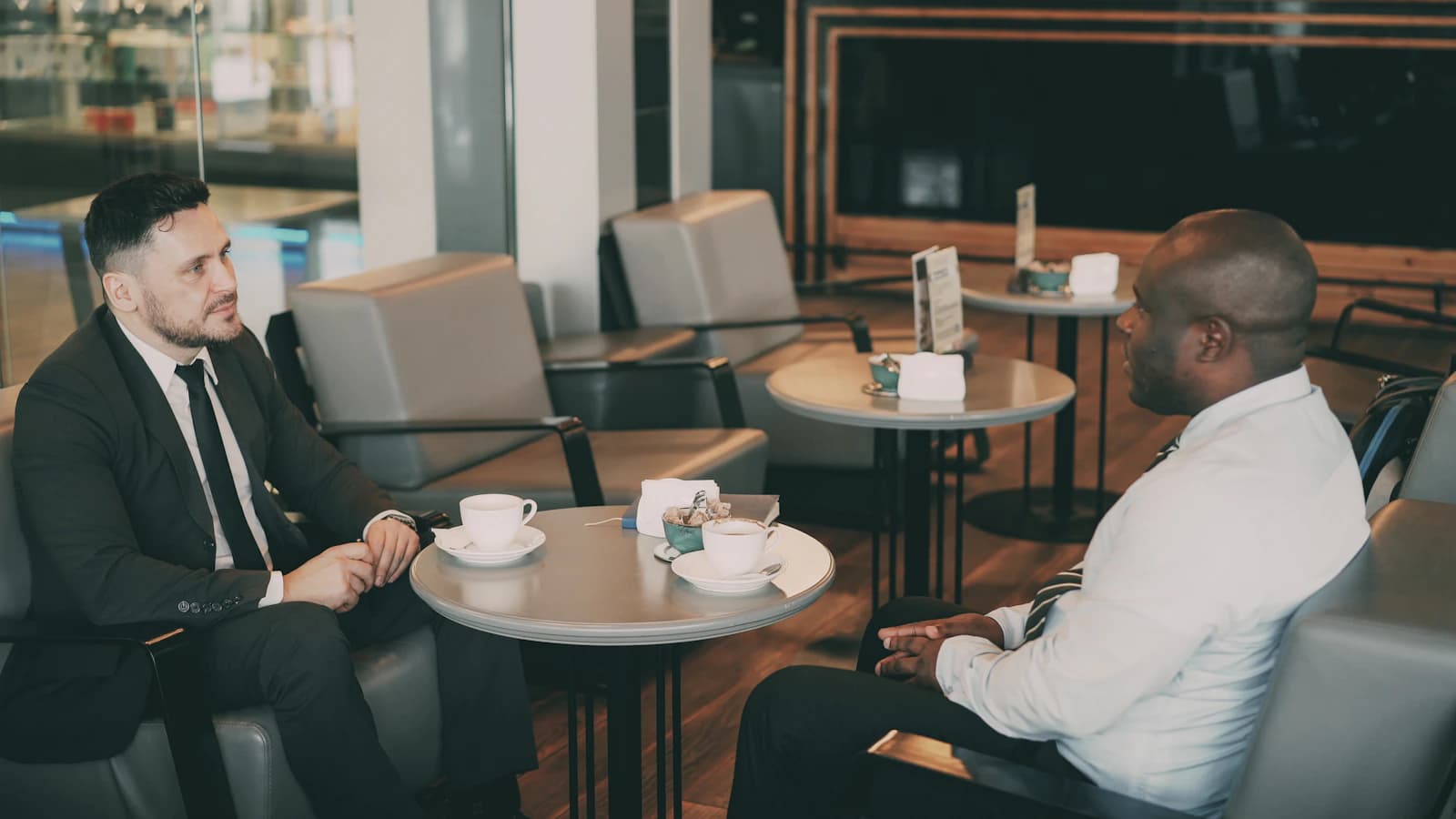 Two men in suits talking over coffee at a café table